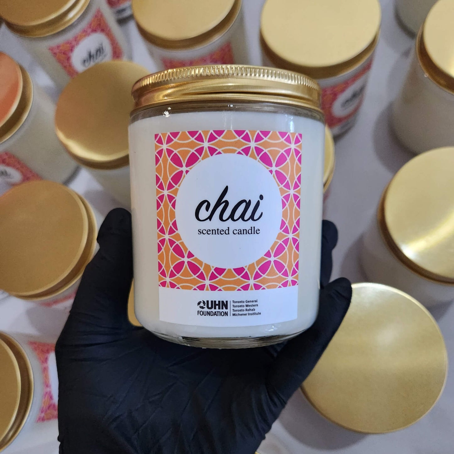 Candle jar labeled 'chai' held by a gloved hand with more candles in the background