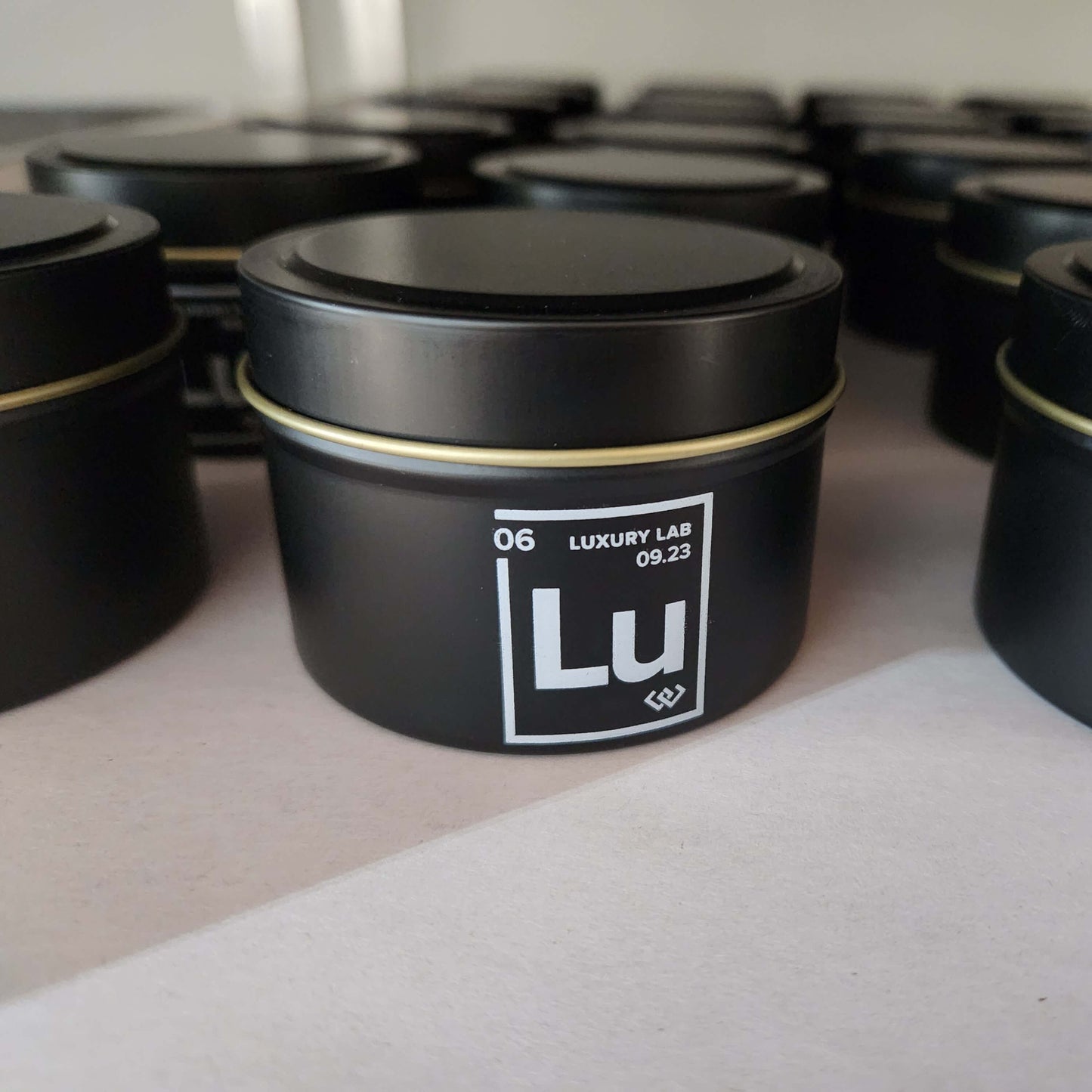 Bulk order of 4oz matte black tin candles with logo imprint for corporate gifting in production.