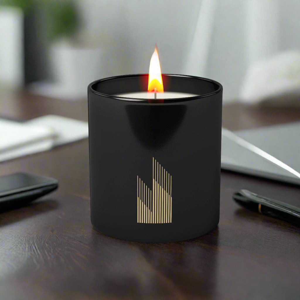 Close-up of single-color logo imprint on a 6oz matte black glass candle on a desk.